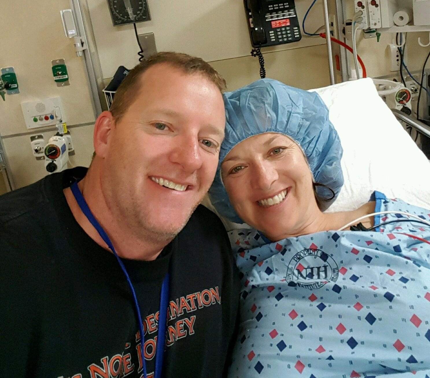 Melinda on her hospital bed, smiling, with her husband at her side, also smiling